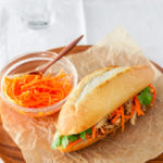 Roasted chicken banh mi sandwich with pickled carrots and cilantro on a wooden plate.