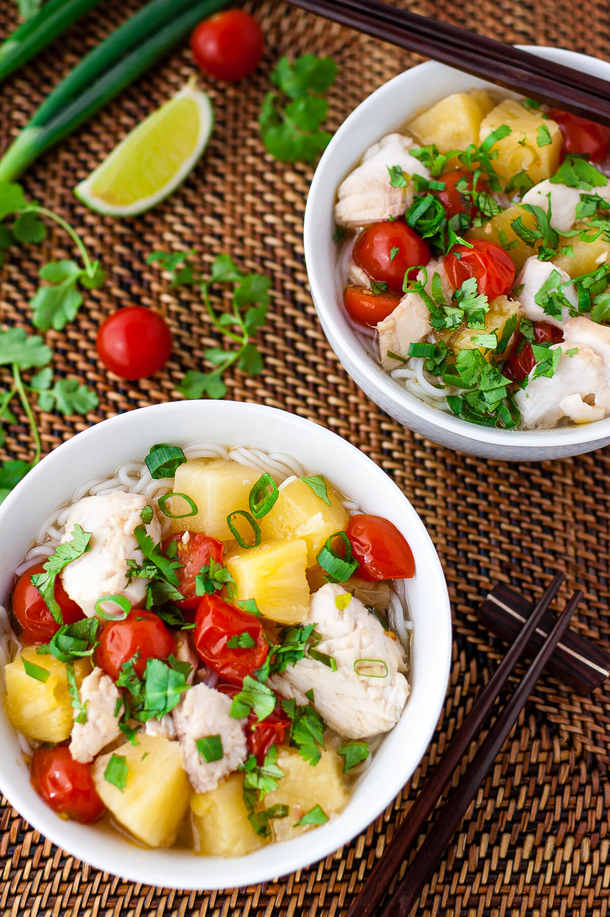 Overhead shot of 2 bowls of Vietnamese fish, pineapple, and tomato soup sprinkled with chopped green onions and cilantro.