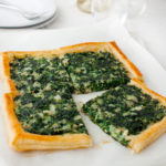 A spinach tart cut into four pieces on a marble board