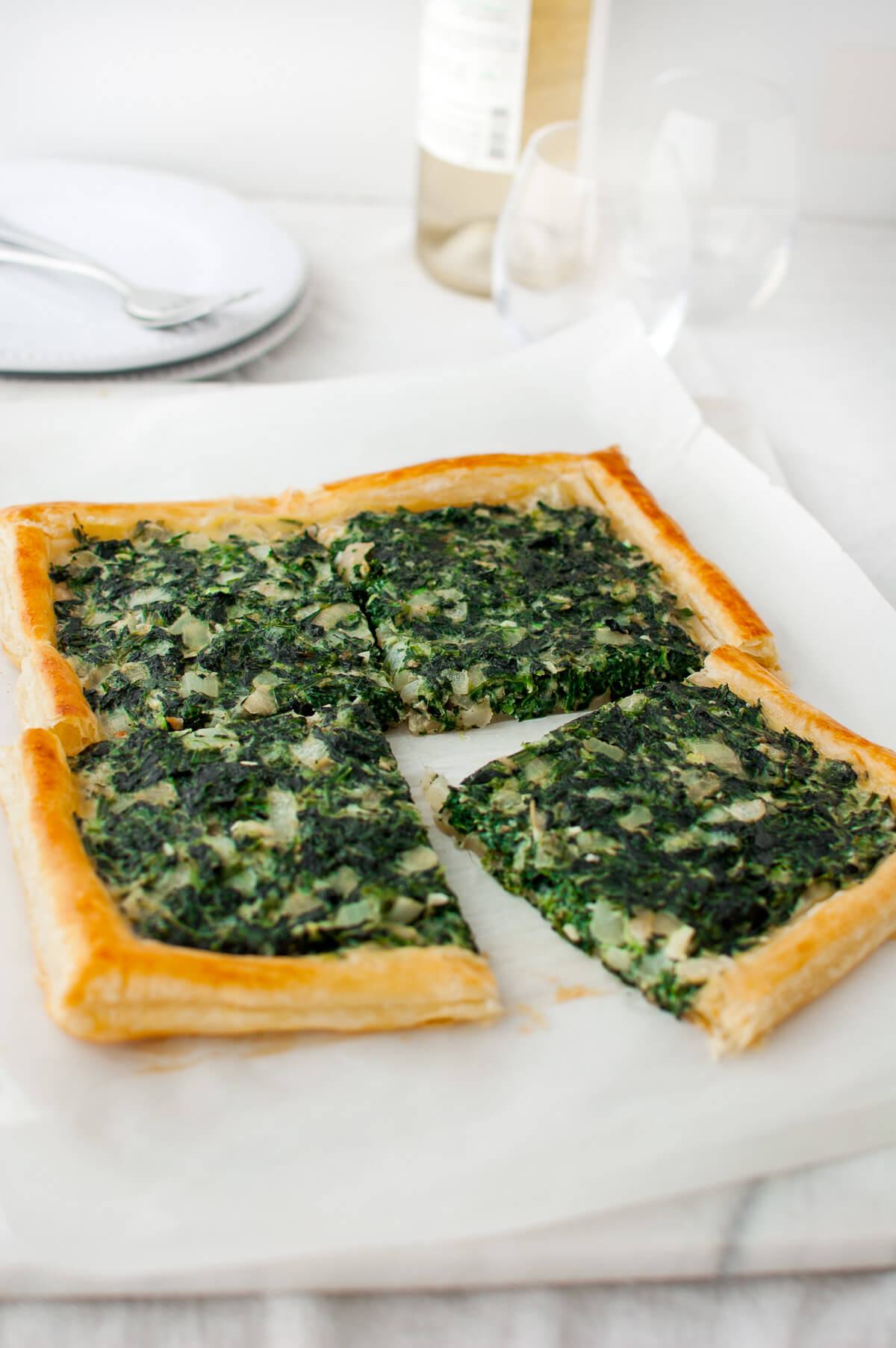 A spinach tart cut into four pieces on a marble board