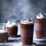 Small glasses of homemade chocolate pudding topped with whipped cream and cookie crumbs.