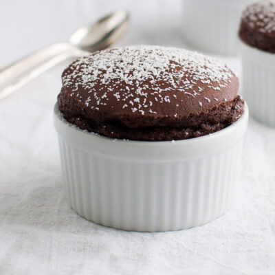 Several chocolate soufflés in small white ramekins sprinkled with powdered sugar.