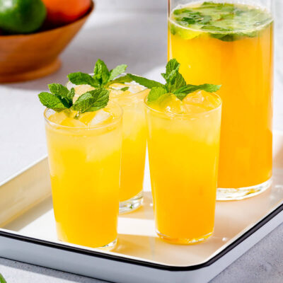 Three glasses and a pitcher of mintade on a white tray.