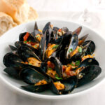 Close-up of some cooked mussels in a white a bowl.