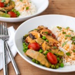 Two plates of vegetable curry with snow peas, mushrooms, and tomatoes served with rice.