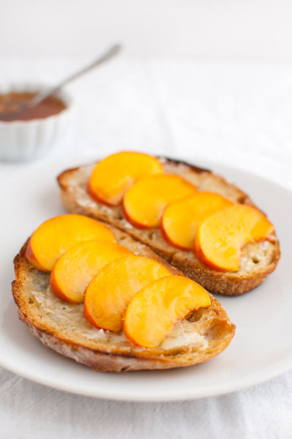 Peach slices on toasted bread on a white plate next to a bowl of honey.