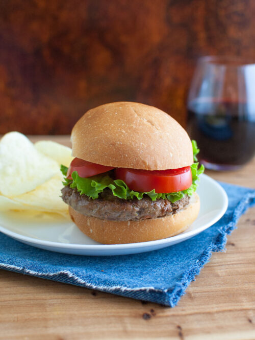 A burger on a white plate with a blue napkin.