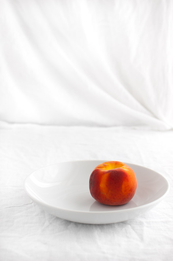 A peach in a white bowl.