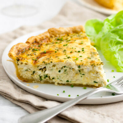 Close-up of a slice of crab quiche on a white plate.