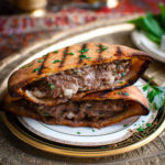 Grilled lamb burger in a pita on a china plate.