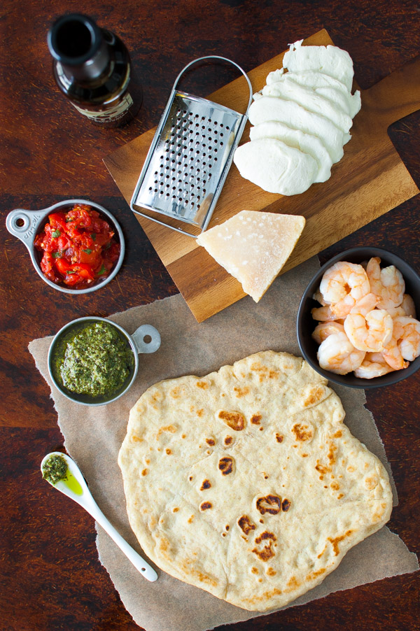 Mozzarella cheese, tomato sauce, pesto, shrimp, and pizza crust on a wooden tabletop.