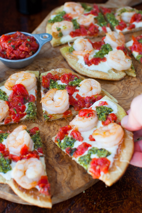 A hand picking up a piece of shrimp pizza.