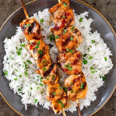 Some grilled chicken skewers on a bed of white rice on a gray plate.