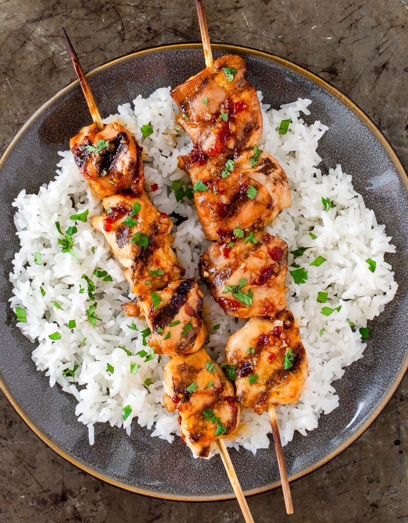 Some grilled chicken skewers on a bed of white rice on a gray plate.