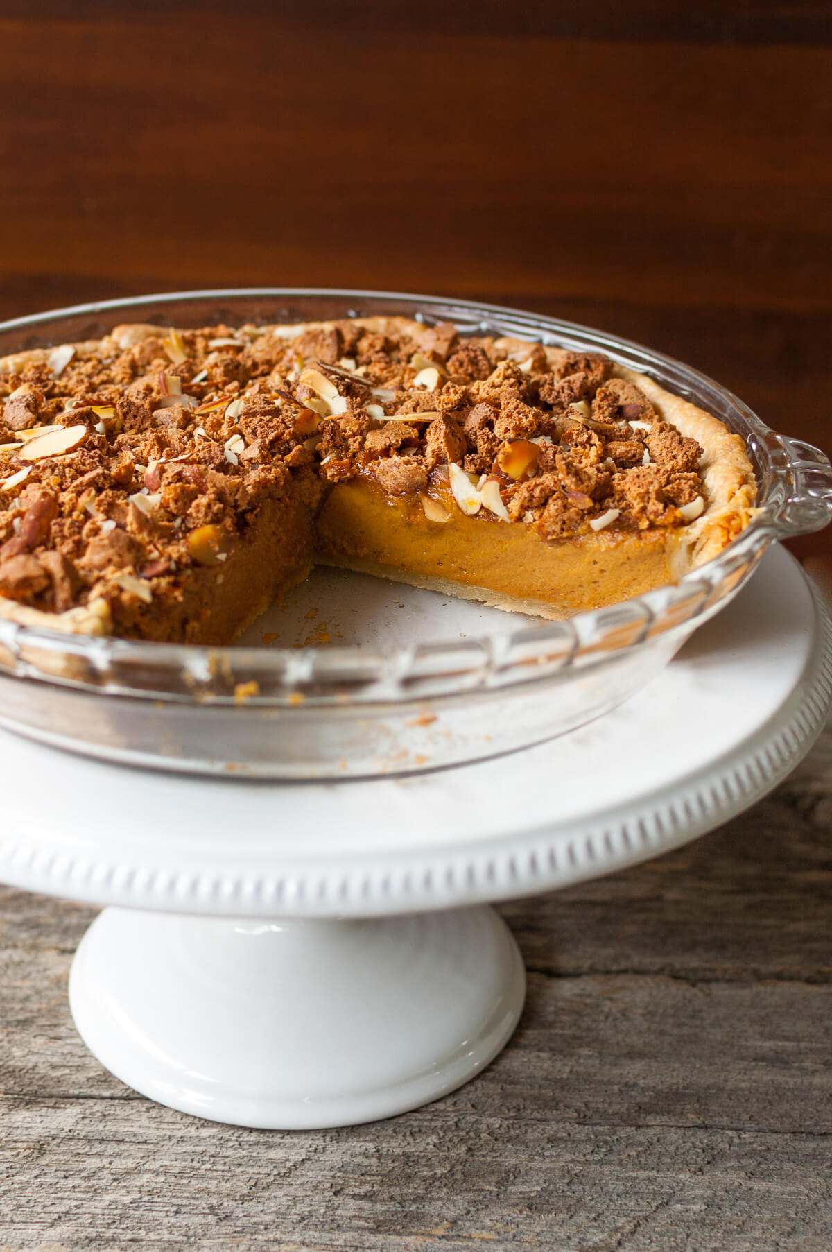 Pumpkin pie with a pie taken out on a white cake stand .