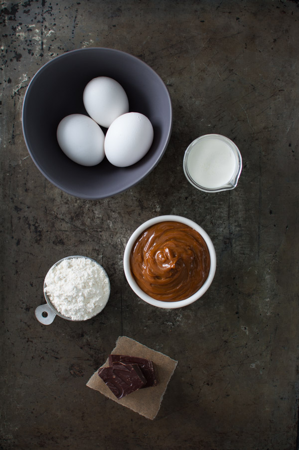 Ingredients to make Molten Chocolate and Dulce de Leche Cake - eggs, cream, flour, chocolate, and dulce de leche on a metal surface.