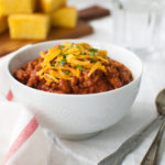 A bowl of chili topped with grated cheddar cheese.