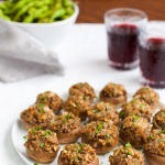 A platter of stuffed mushrooms next to glasses of wine.