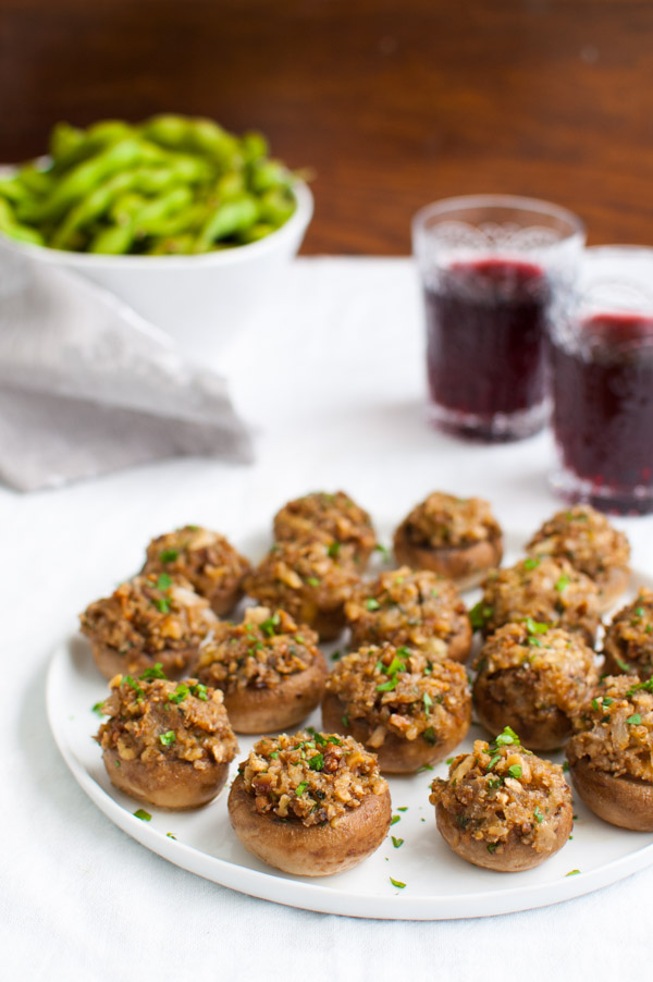 A platter of stuffed mushrooms next to glasses of wine.