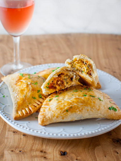 Turkey empanadas on a plate next to a glass wine.