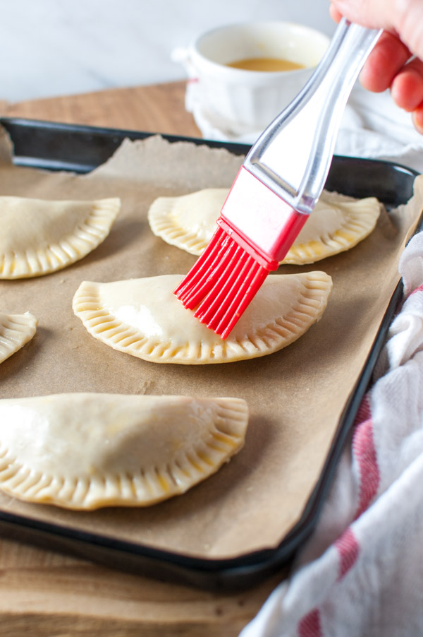 Empanadas being brushed with an egg wash.