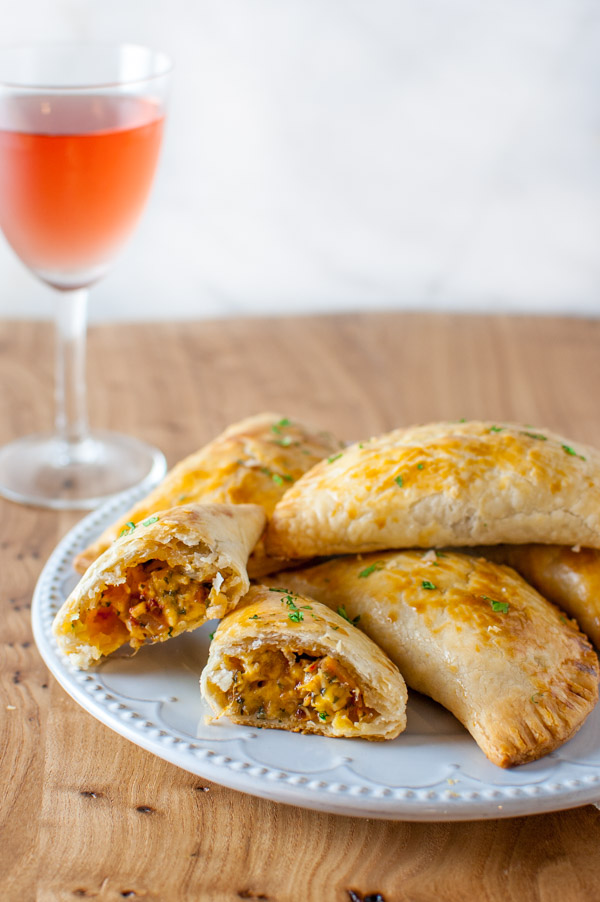 Turkey empanadas on a plate next to a glass wine.