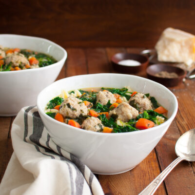 Two bowls of Italian wedding soup on a wooden board.