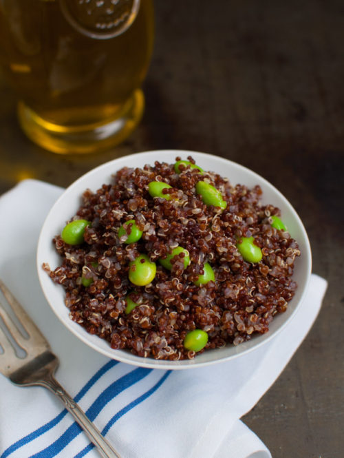 A bowl of red quinoa and edamame salad next to a bottle of olive oil.