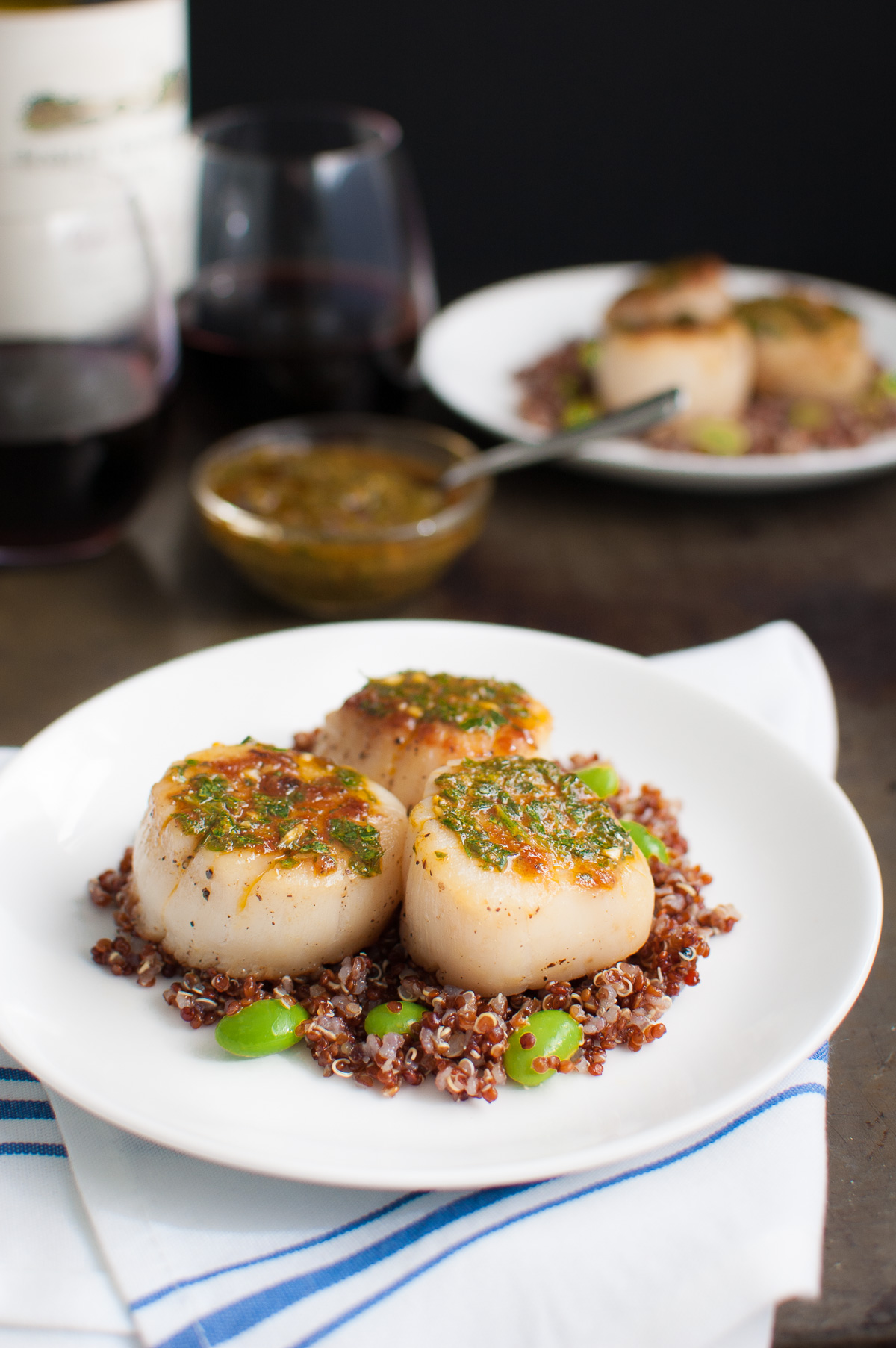 Seared scallops topped with chermoula served with some red quinoa on a white plate.