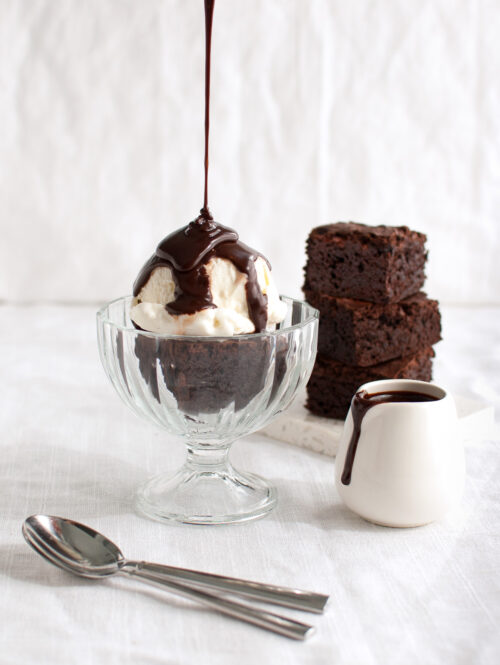 Chocolate sauce being poured on a brownie sundae.