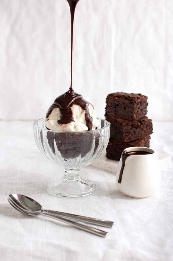 Chocolate sauce being poured on a brownie sundae.