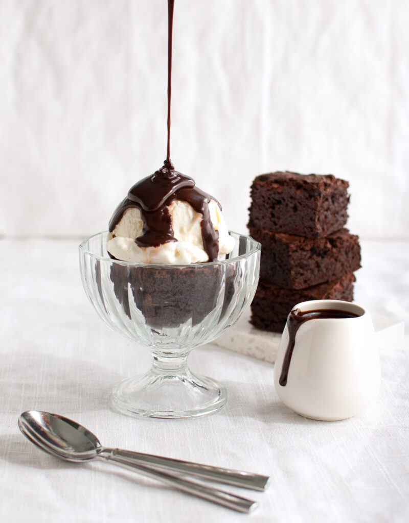 Chocolate sauce being poured on a brownie sundae.