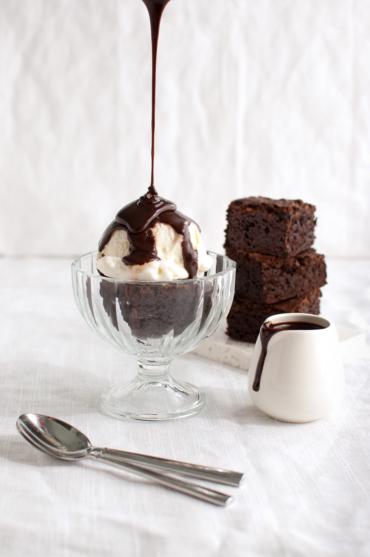 Chocolate sauce being poured on a brownie sundae.