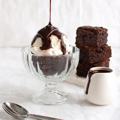 Chocolate sauce being poured on a brownie sundae.