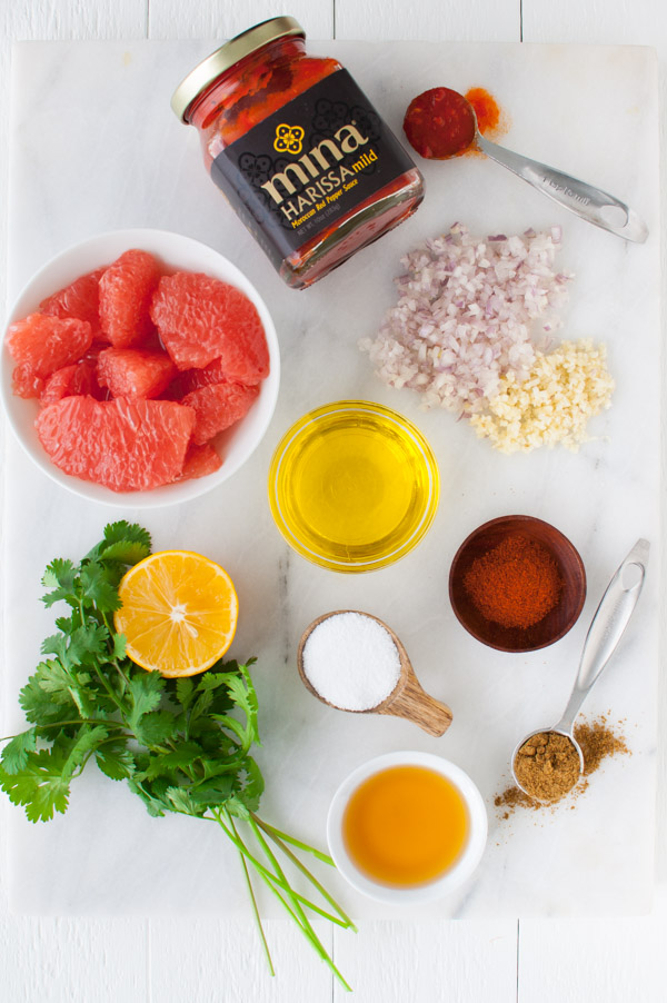 Grapefruit segments, lemons, harissa paste, cilantro, shallots, garlic, and spices on a marble board.