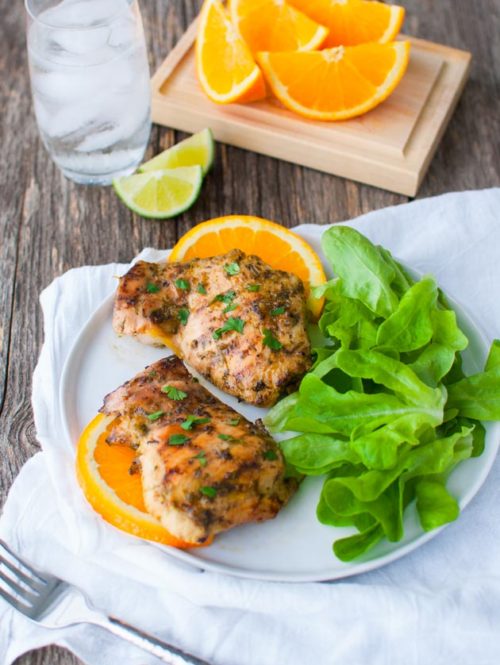 Grilled chicken with orange slices and a green salad on a plate.