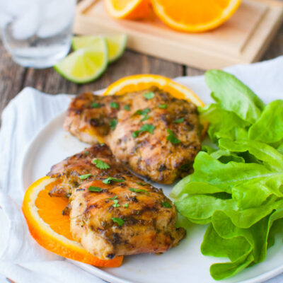 Grilled chicken with orange slices and a green salad on a plate.