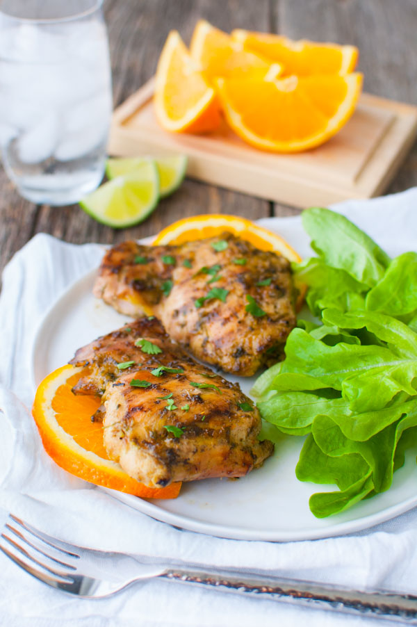 Grilled chicken with orange slices and a green salad on a plate.