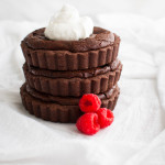 A stack of three chocolate raspberry tartlets garnished with some whipped cream and fresh raspberries.