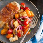 Prosciutto wrapped chicken cutlets next to a tomato, bread, and onion salad.