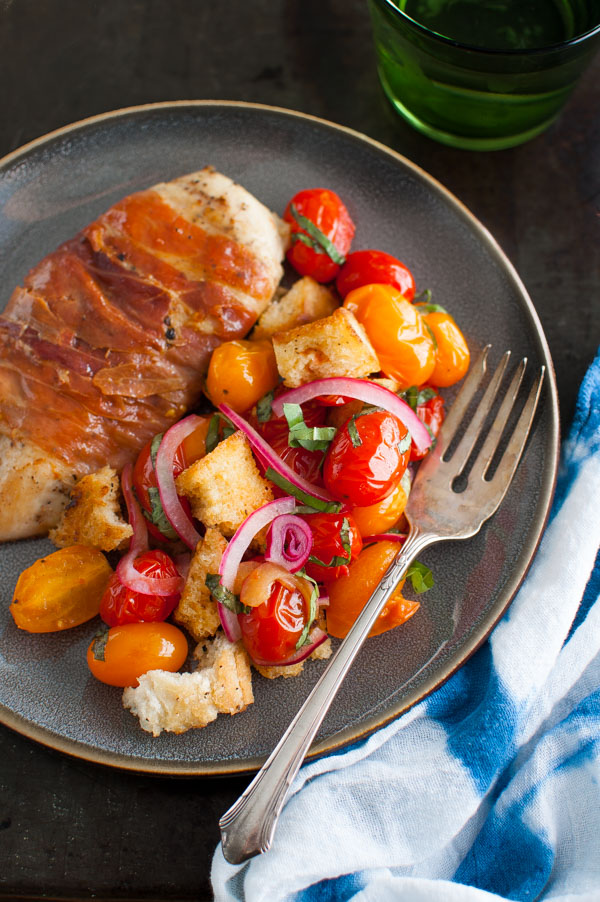 Prosciutto wrapped chicken cutlets next to a tomato, bread, and onion salad.