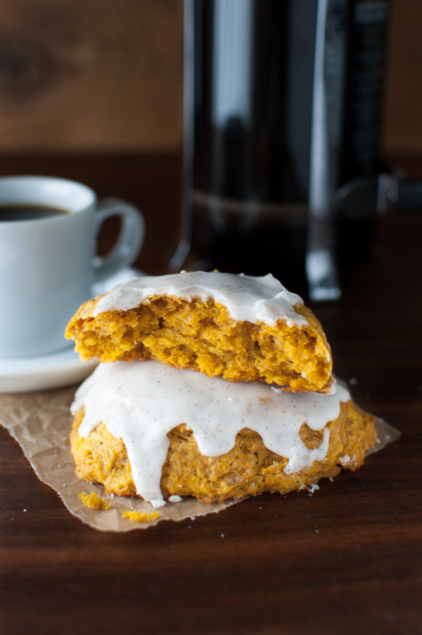 A stack of pumpkin scones with vanilla glaze on some brown parchment paper next to a coffee cup.