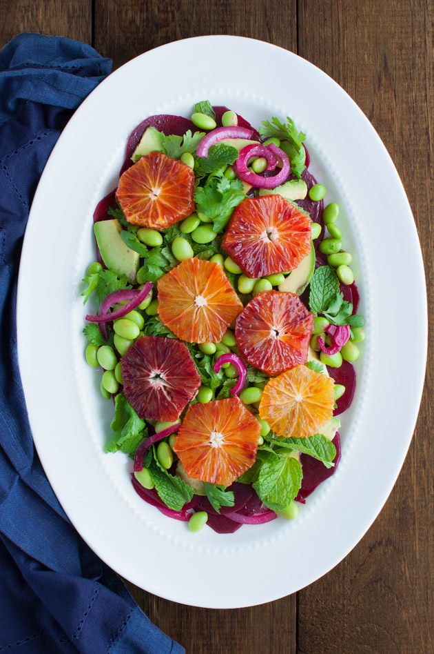 Beets, avocado, edamame, and blood orange salad on a white plate.