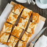 Several slices of marbled pumpkin cheesecake bars on a serving board.