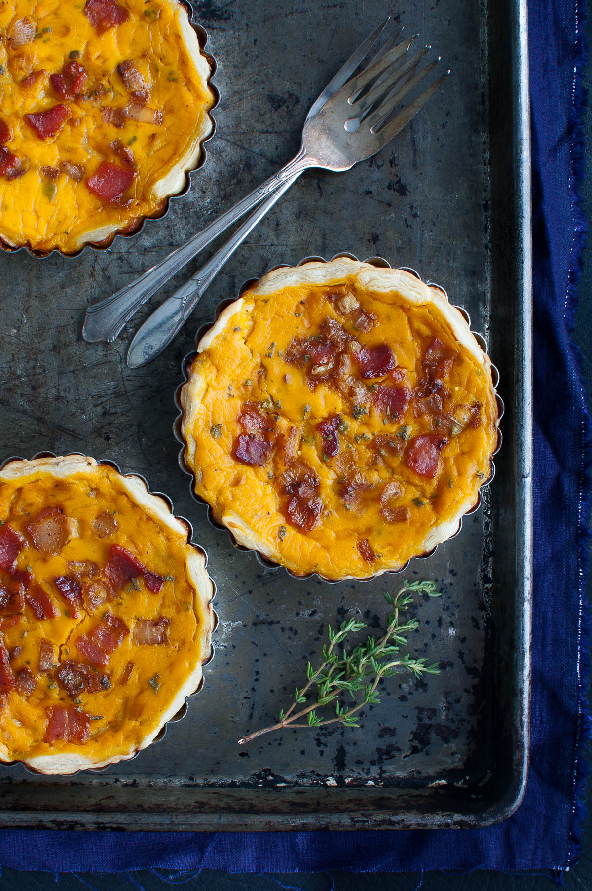 Three squash tarts and two forks on a metal tray.