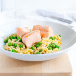 Plate of parmesan orzo with salmon and peas in a white bowl.