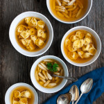 Several bowls of tortellini in brodo on a wooden background.