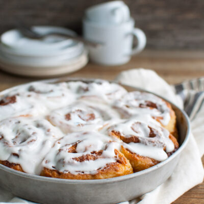 A pan of iced cinnamon rolls on a wooden table top.