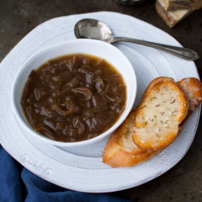 A bowl of French onion soup next to some cheese crostini.