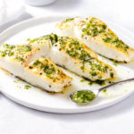 Roasted halibut topped with cilantro-lime sauce on a white plate.